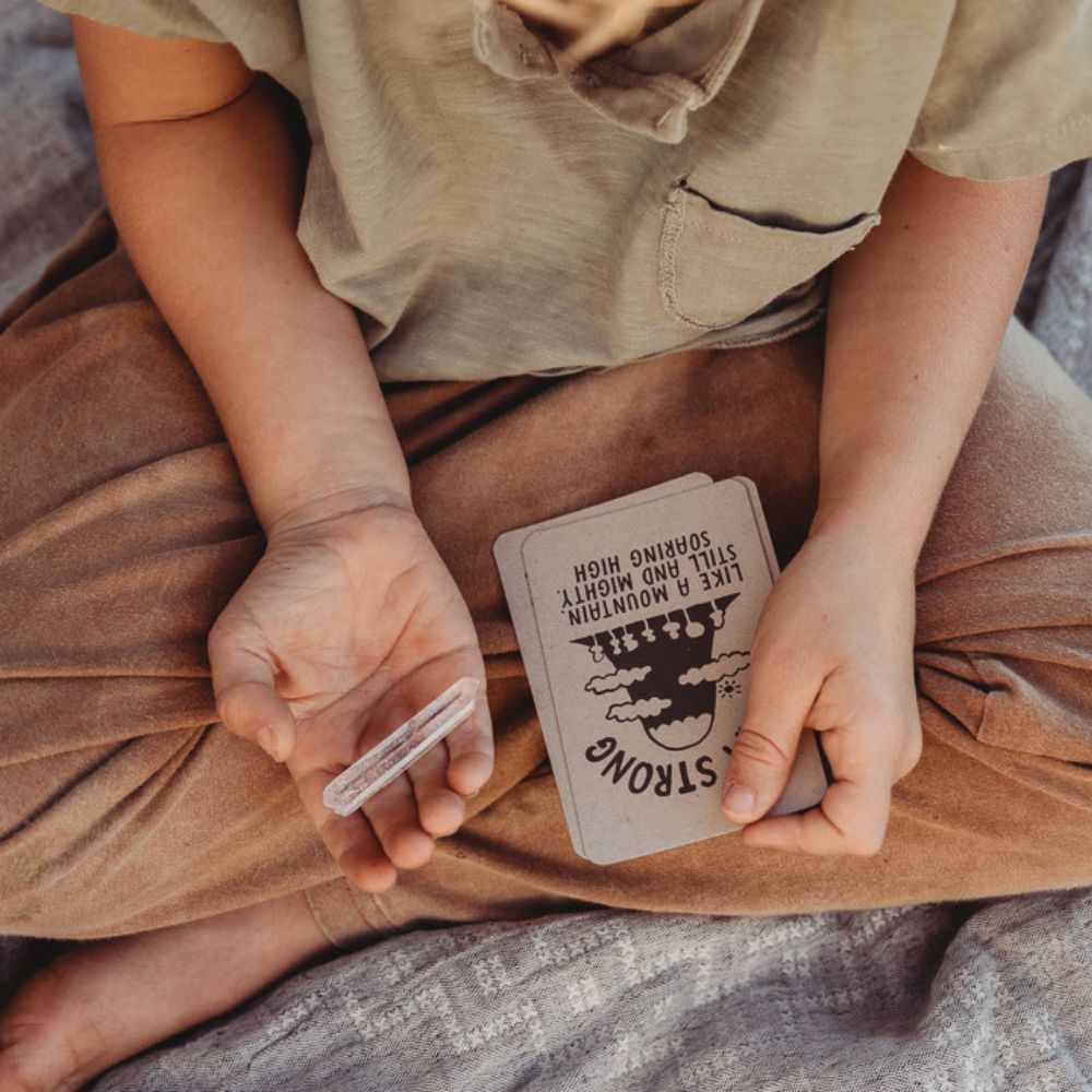 Boy sitting cross-legged holding Affirmation Cards and a crystal.