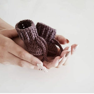 Pair of chocolate knitted baby booties being held in hands
