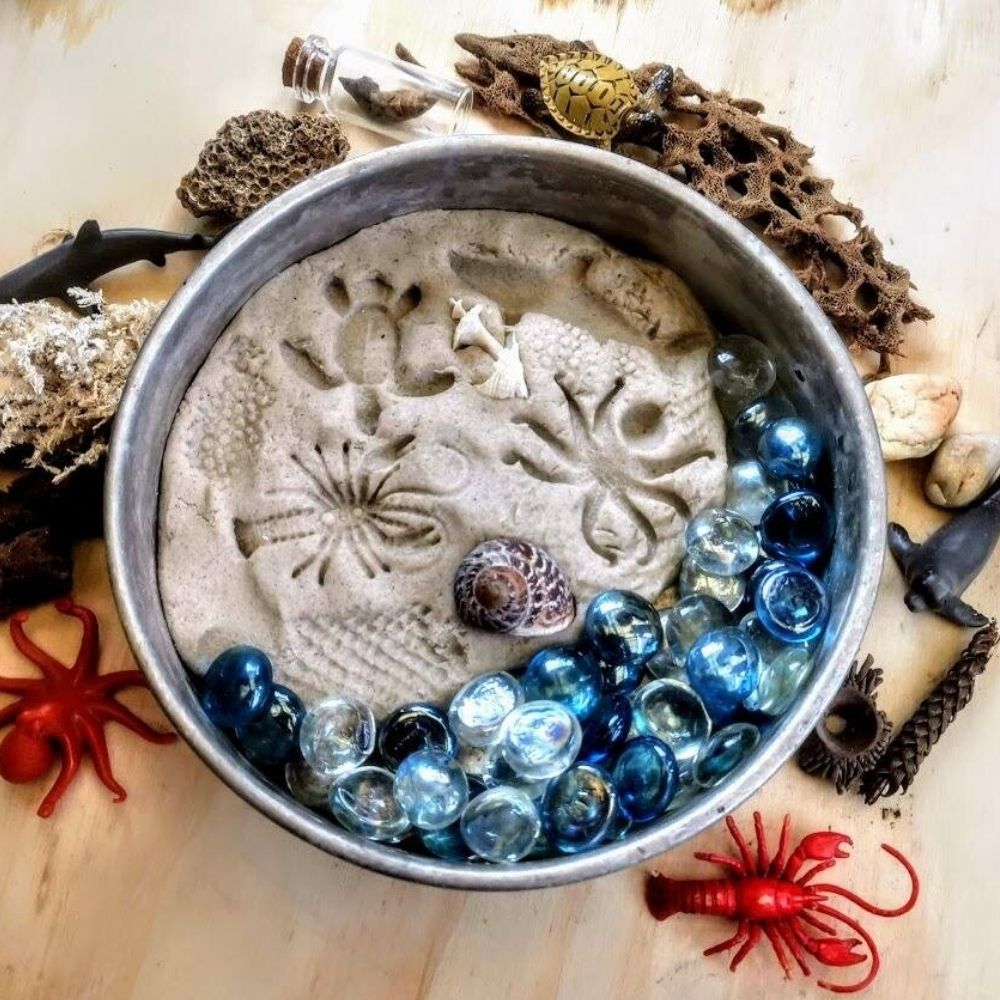 Aerial view of a bowl filled with Sand Playdough, blue pebbles and a shell.