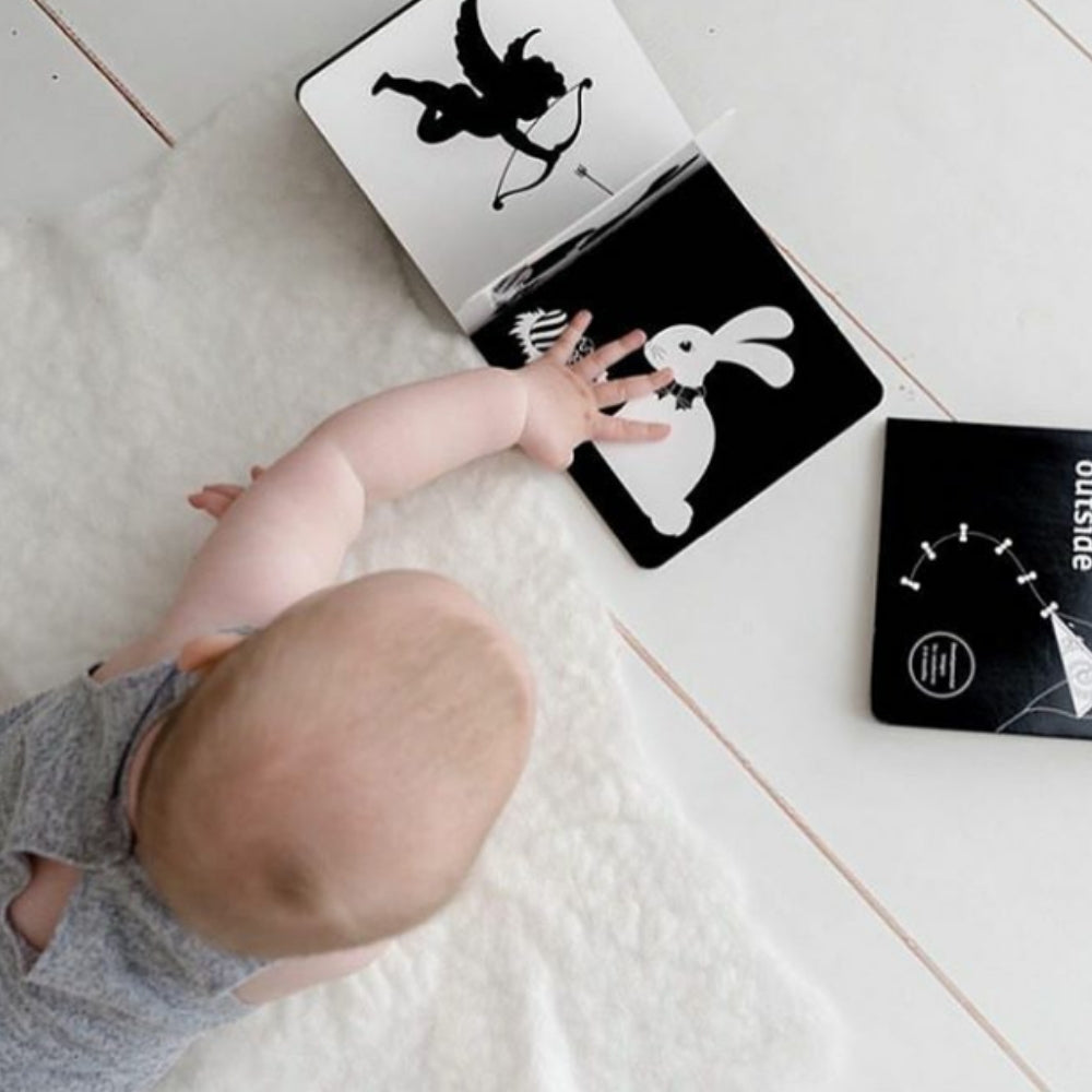 baby on tummy on the floor reading a black and white book