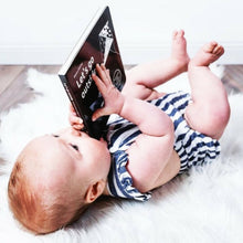 Load image into Gallery viewer, baby boy lying on floor holding a board book and chewing on a corner
