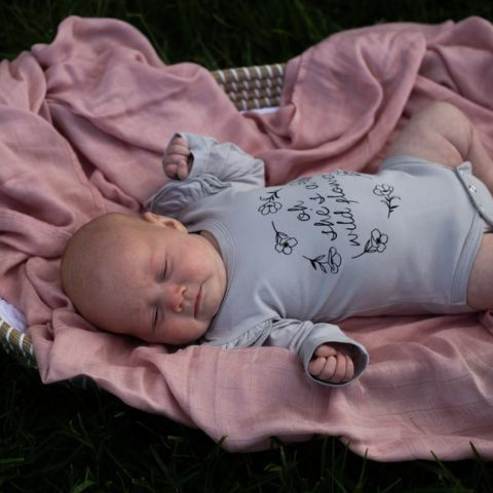 baby-girl-in-wildflower-fluttersuit-lying-on-a-pink-blanket-in-a-basket